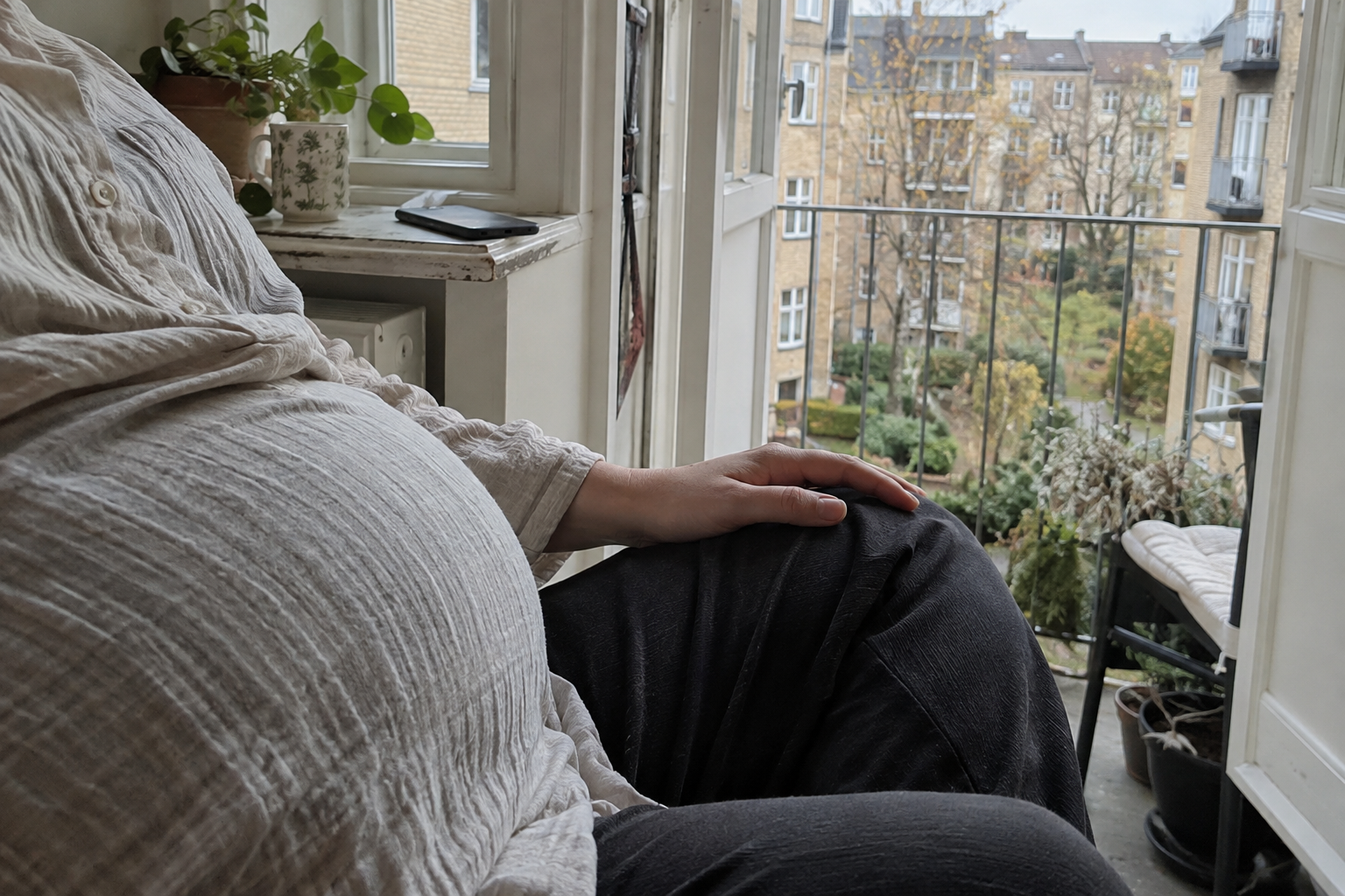 En gravid kvinde tager en pause ved en åben altandør med telefonen lagt væk